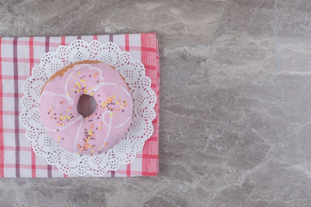 Glazed donut on a doily on a towel on marble