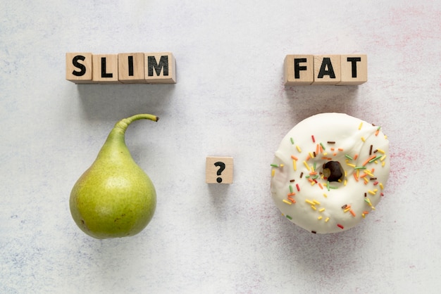 Free photo glazed donut; pear and slim; fat text with question mark on wooden block over concrete surface