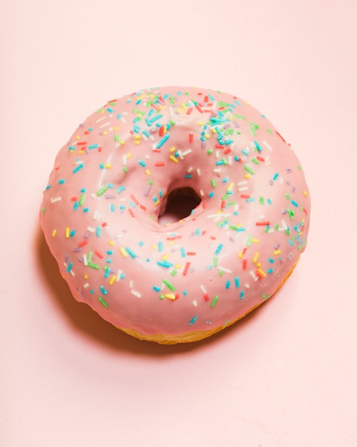 Glazed donut with sprinkles on pink surface