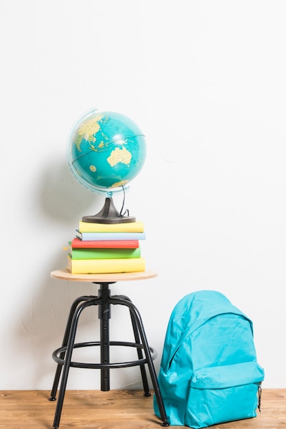 Globe on books placed on stool chair next to schoolbag 