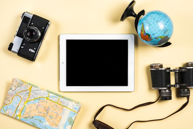 Globe; camera; map; binocular and digital tablet on beige background
