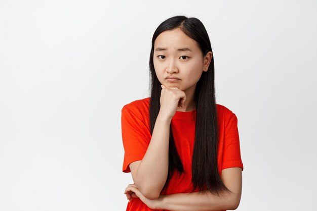 Gloomy asian woman looking at camera troubled listening to something upsetting being distressed standing over white background