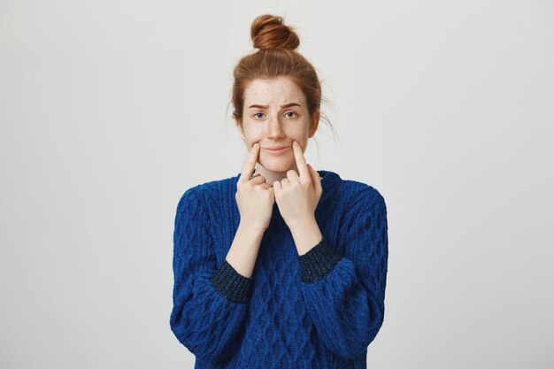 Gloomy redhead girl pulling smile to hide sadness