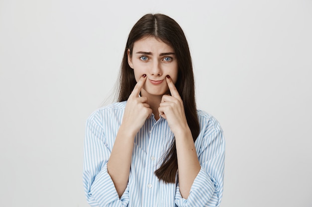 Gloomy woman making smile with fingers on corner of lips