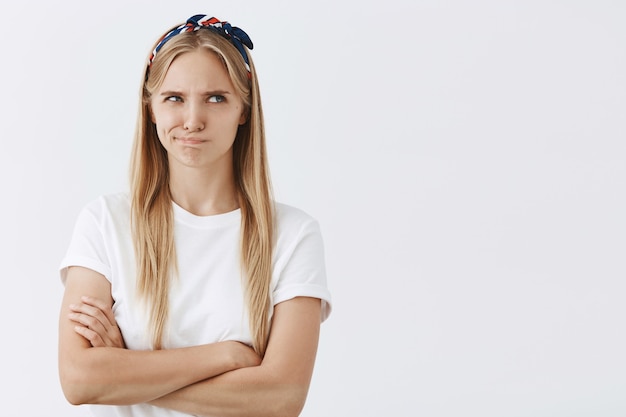 Gloomy young blond girl posing against the white wall