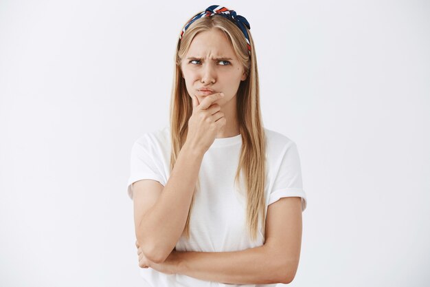 Gloomy young blond girl posing against the white wall