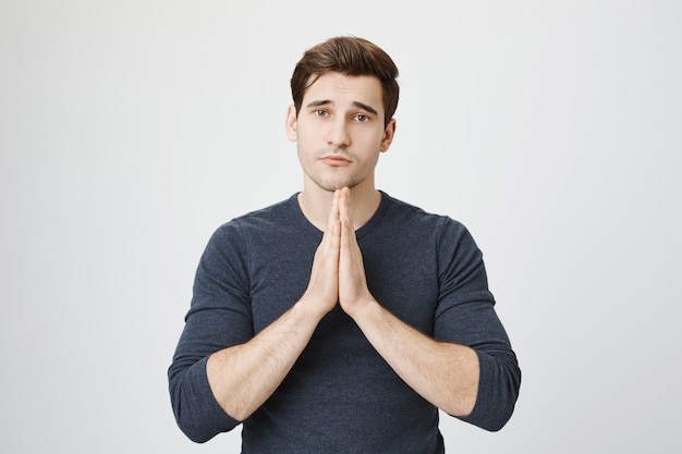gloomy young man asking apology, pleading for mercy with hands in pray