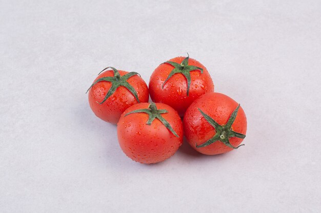 Glossy red tomatoes on white surface