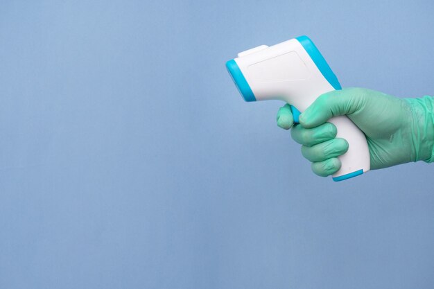 Gloved hand of a healthcare worker holding a thermometer isolated on blue