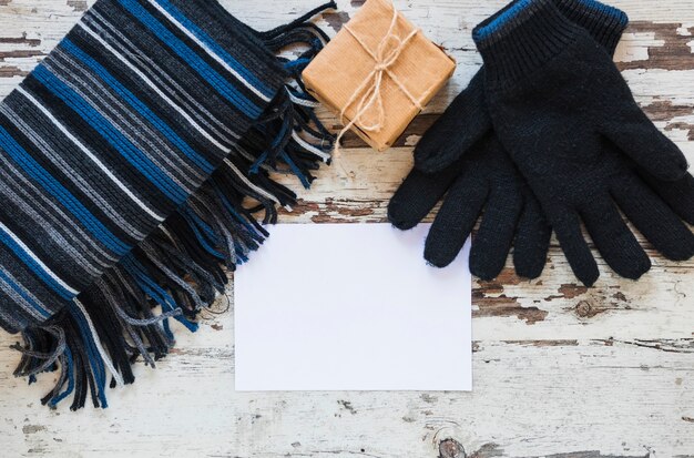 Gloves and scarf near gift and paper sheet