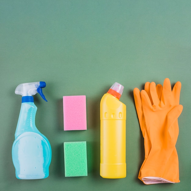 Gloves, sponge and plastic bottles on green background