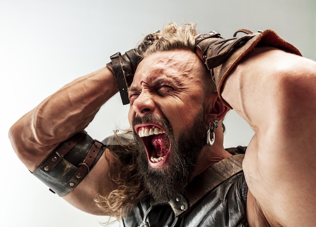 God of thunder. Blonde long hair and muscular male model in leather viking's costume with the big hammer cosplaying isolated on white studio background. Fantasy warrior, antique battle concept.