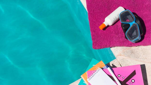 Goggles with lotion on towel near books and pool