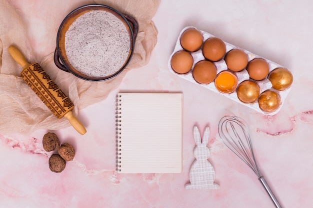 Бесплатное фото Золотые пасхальные яйца в подставке с блокнотом, кухонной утварью и кроликом