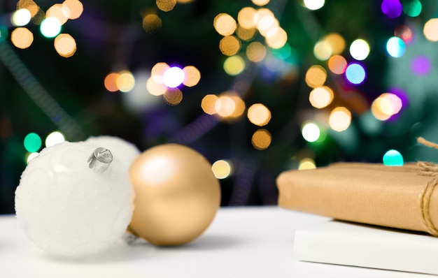 Gold and white balloons on a wooden table with gifts and a festive fir tree in the background