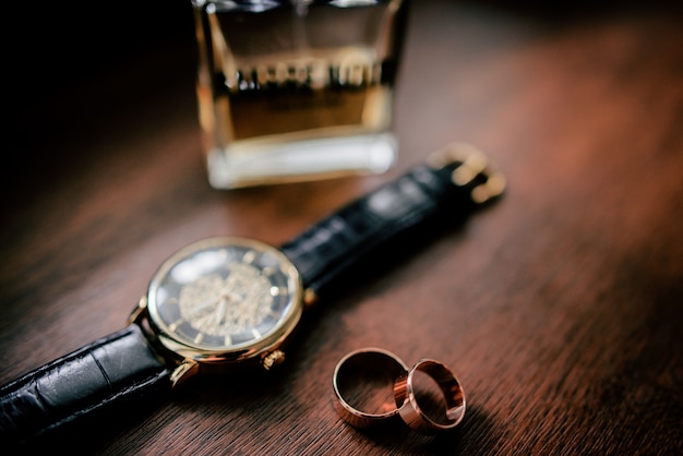 Free photo golden cufflings, wedding rings and watch lie on wooden table
