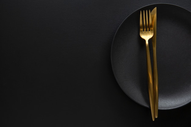 Golden cutlery with textile on plate on dark background. Top View.