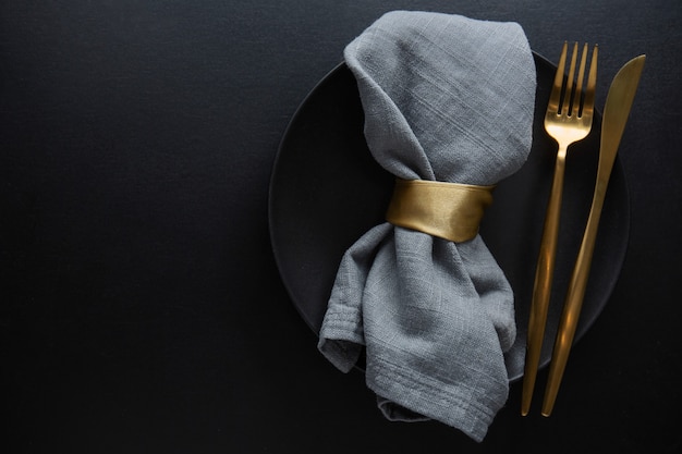 Golden cutlery with textile on plate on dark background. Top View.