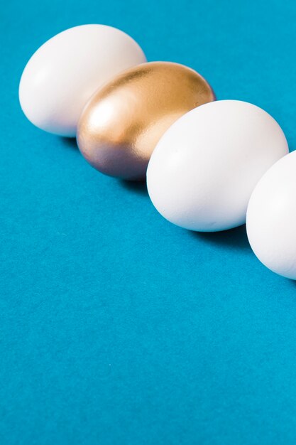 Golden egg standing out from white eggs on blue background