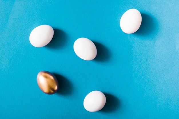 Golden egg and white eggs on blue background