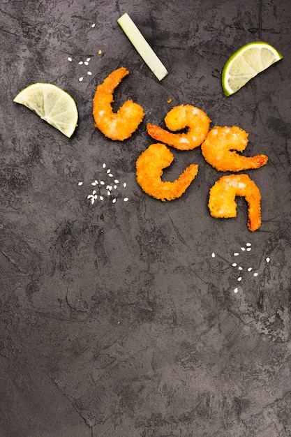 Free photo golden fried shrimps with sesame seeds and lemon wedges over rough black surface