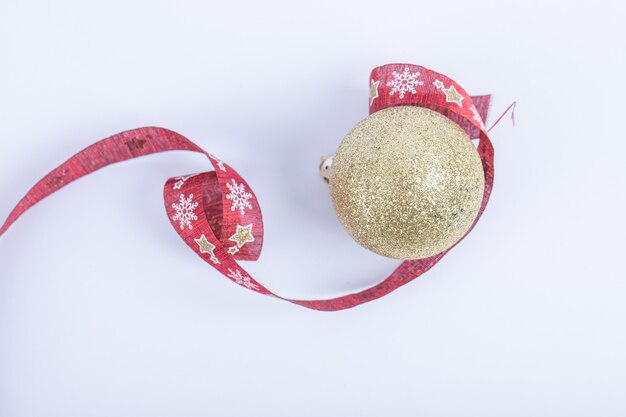 A golden glittering ball with red Christmas ribbon on the white