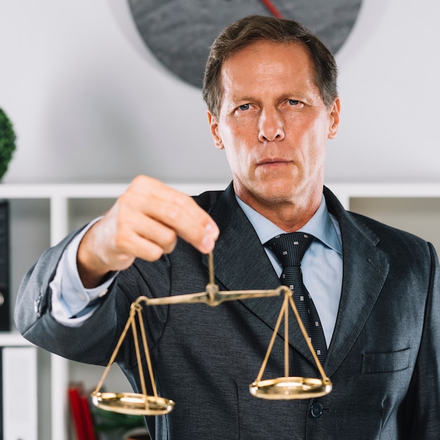Golden justice scale behind the lawyer signing the document on desk
