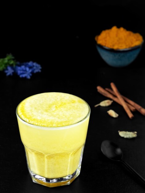 Golden milk with turmeric and other spices on a black surface