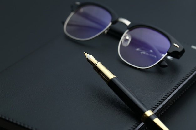 golden pen,notebook,calculator and glasses on black desk