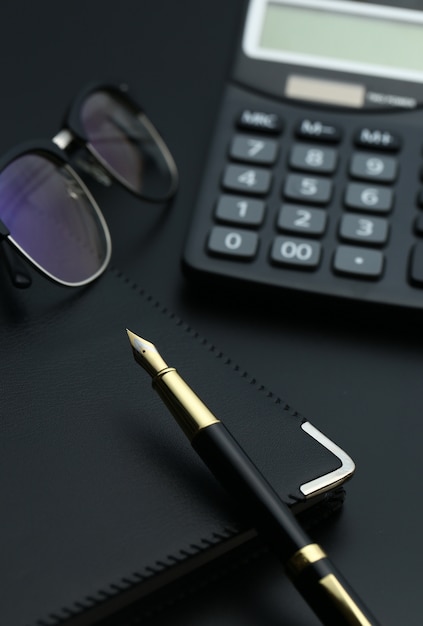 황금 펜, 노트북, 계산기 및 검은 책상에 안경