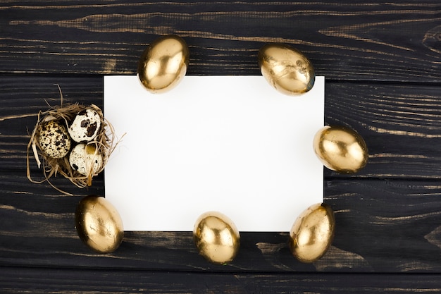 Golden and quail eggs around paper sheet