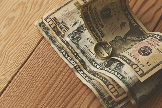 golden ring on some dollar bills on a wooden surface