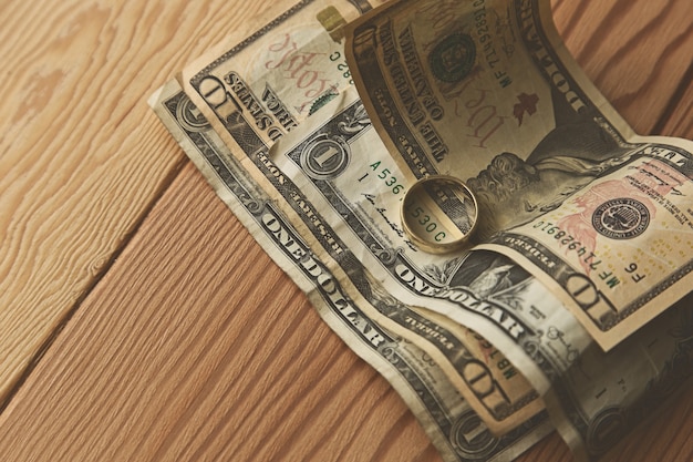 golden ring on some dollar bills on a wooden surface