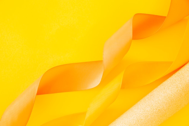 Golden rolled up paper and curled ribbon on yellow background