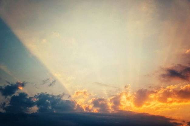 Золотой закат на фоне голубого неба, яркие солнечные лучи проходят сквозь облака Premium Фотографии