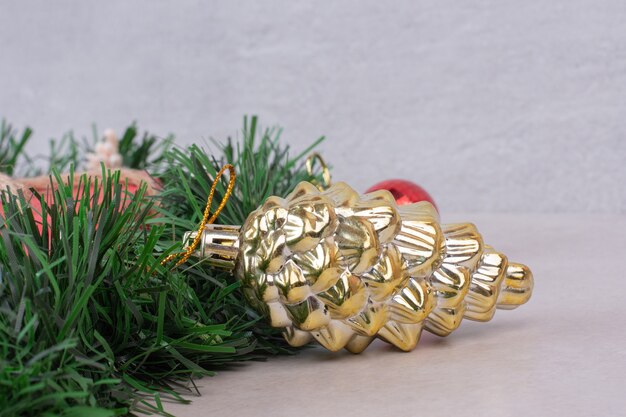 Golden toy of pinecone on green tinsel on white surface