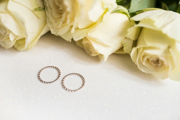 Golden wedding rings and fresh roses on white background