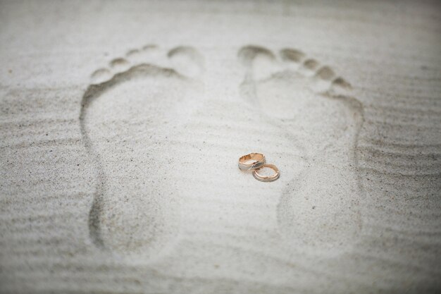 Golden wedding rings lie between footsteps on the beach 