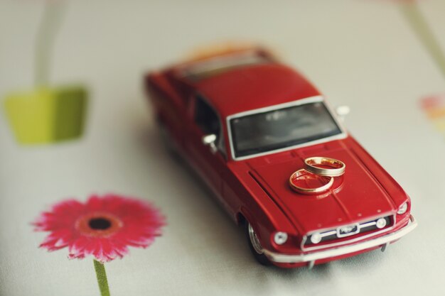 Golden wedding rings lie on a toy red Mustang 