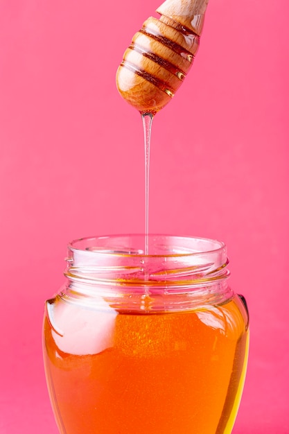 Goney dripping off dipper in jar pink background