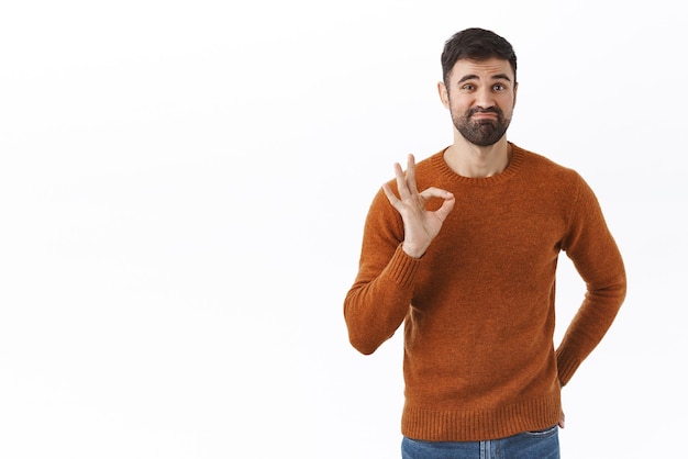 Good but not the best Portrait of skeptical bearded male boss show opinion product is average quality smirk and show okay sign as agree not bad approve thing stand white background