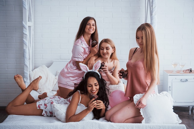 좋은 음식은 좋은 분위기를 만듭니다. 귀여운 소녀들은 흰 벽과 침대가있는 멋진 조명이있는 방에서 모임과 휴가를 보내고 있습니다. 손에 초콜릿 쿠키