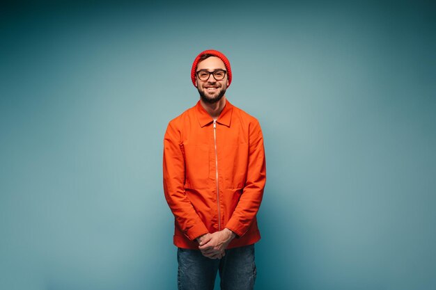 Good humored teenage guy in orange outfit posing on blue background