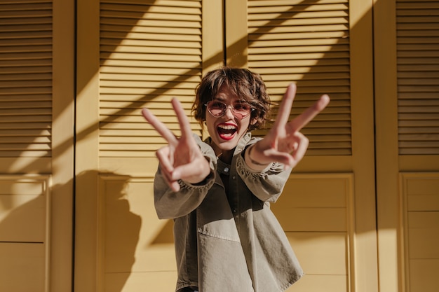 Good-humored woman with red lips showing peace sign