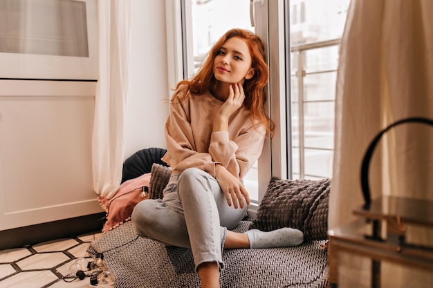 Good-humoured girl with wavy hair posing at home. Indoor photo of cheerful european lady with gentle smile.