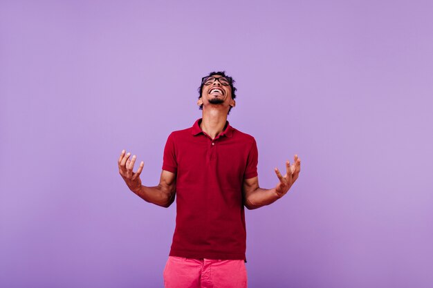 Good-humoured male model in red t-shirt looking up. Optimistic african young man having fun.