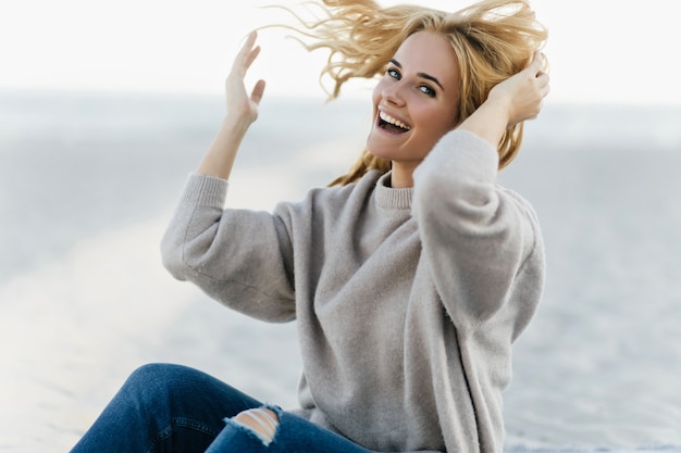 Free photo good-humoured woman having fun at sea coast in autumn weekend. outdoor portrait of caucasian funny woman laughing in nature