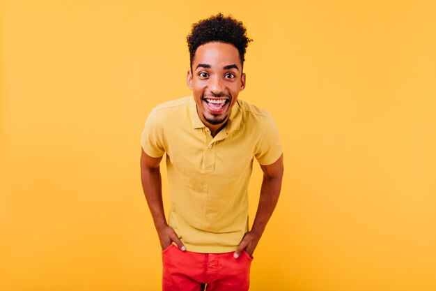 Good-humoured young man with dark curly hair expressing happiness. Active african boy posing with hands in pockets.