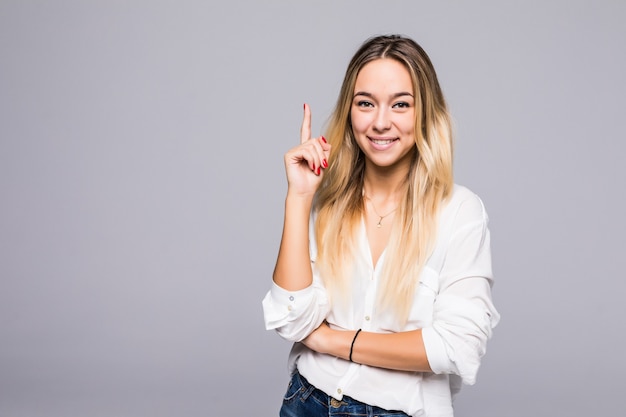 Good idea. Successful smiling woman on grey wall is pointing up with her fingers.