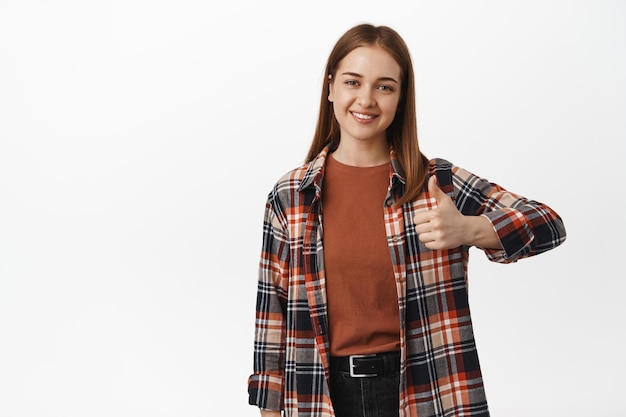 Free photo good job. young smiling woman happy about result, thumbs up in approval, like and agree, support your choice, standing satisfied against white background